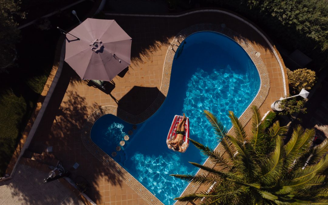aerial shot of a man on a floatie in a fiberglass pool with palm trees